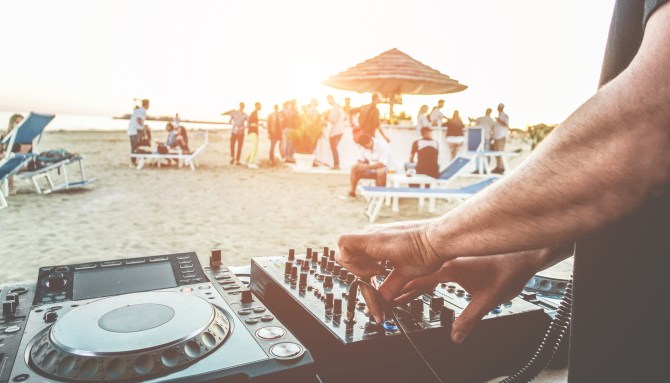 Someone DJing on a beach near dozens of people