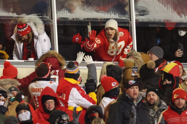 Taylor Swift, in a red jacket and white hat, celebrates with fans at the AFC Wild Card Playoffs