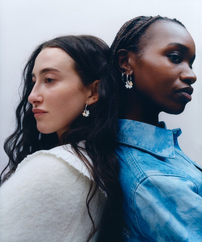 Two models posing back-to-back in Ganni x Mejuri four leaf clover earrings