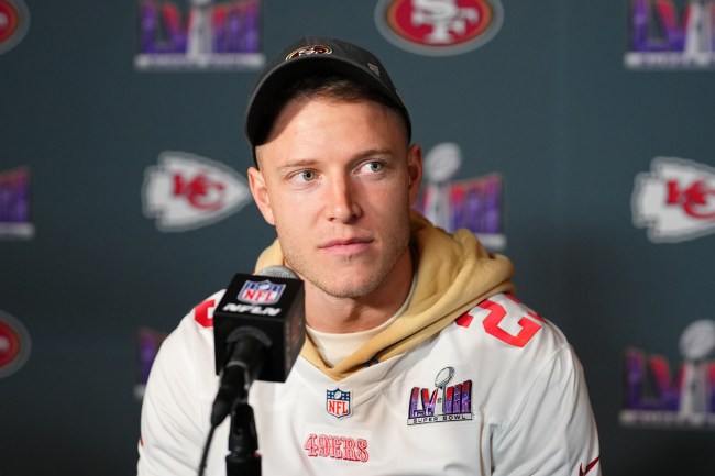 Christian McCaffrey wife. Christian McCaffrey sitting with a microphone in front of him. He's wearing a white 49ers jersey, a beige hoodie, and cap.