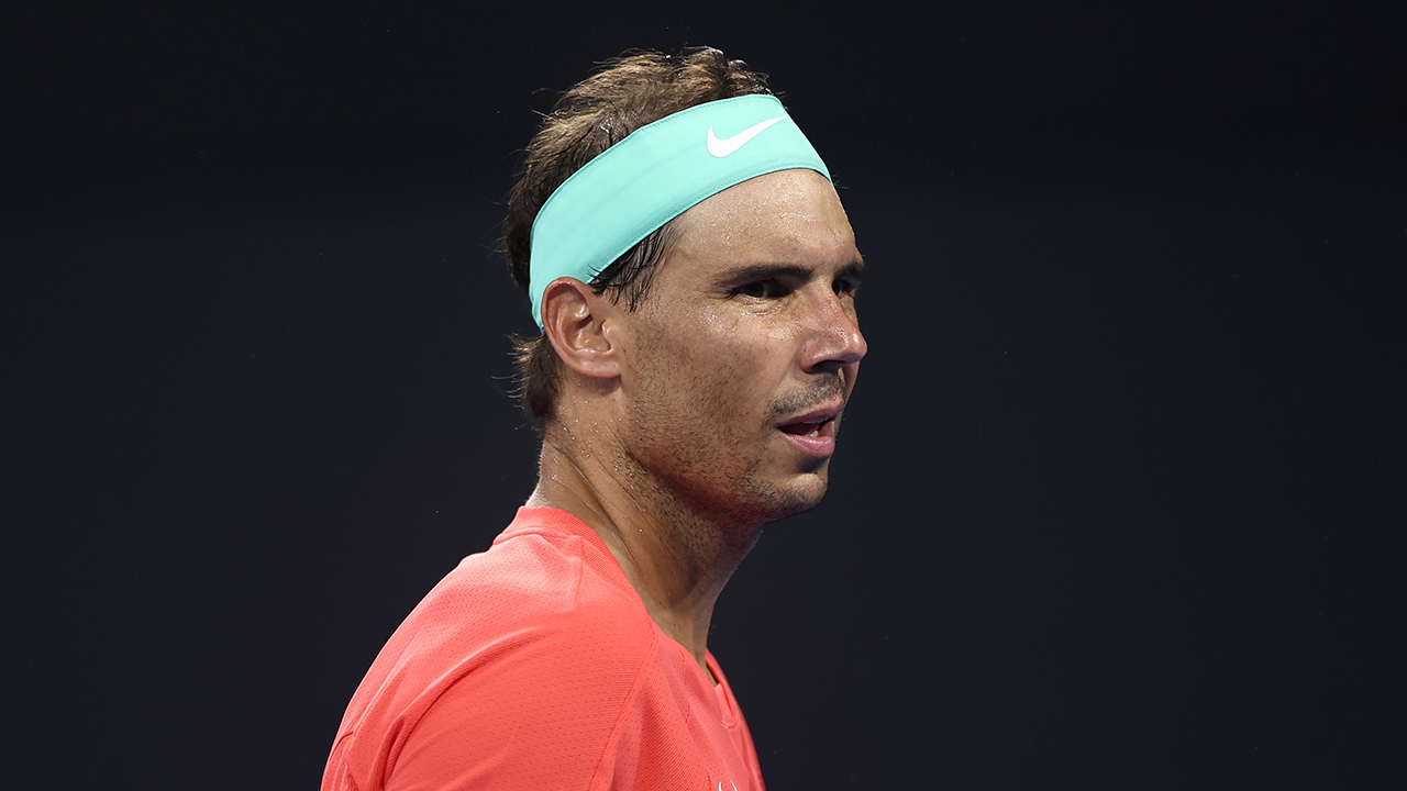 Rafael Nadal Net Worth. Rafael Nadal in a red shirt and blue sweatband.