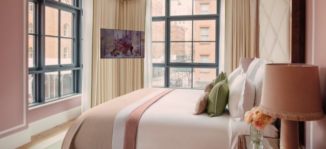 A pink bedroom at Fouquet's hotel, complete with layered bedding, white trim, off-white drapes, and a fringe-lined lampshade