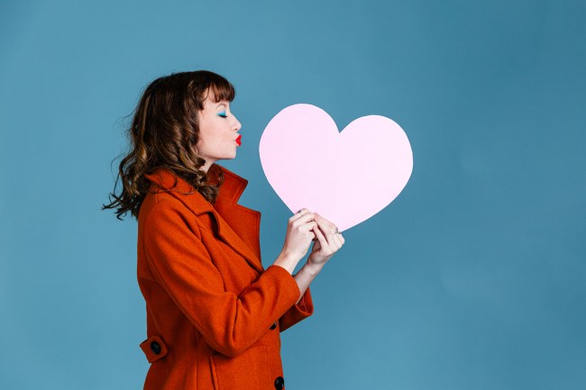 Studio shot of young woman holding pink artificial paper cut out heart shape