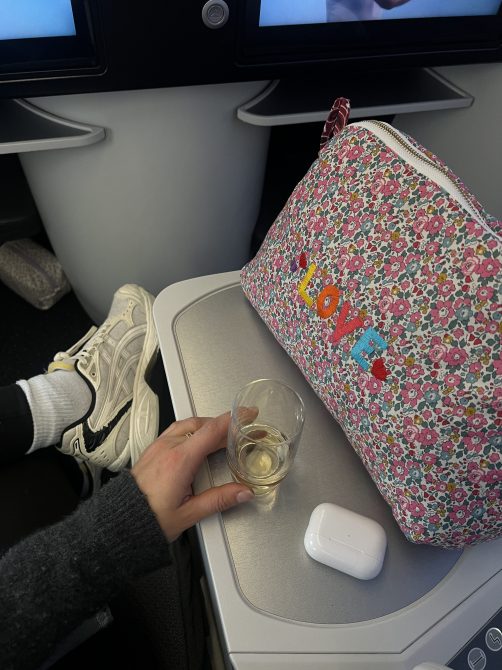 The view from my seat on La Compagnie's plane, featuring a tray table, glass of wine, and my zip-up bag
