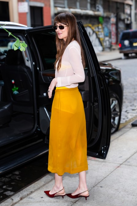 Dakota Johnson wearing a sheer mustard skirt, a white top, and kitten heels.