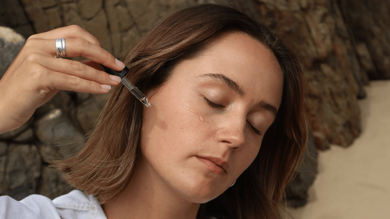 Woman on the beach applying Saya's Super Serum to her face with a dropper.