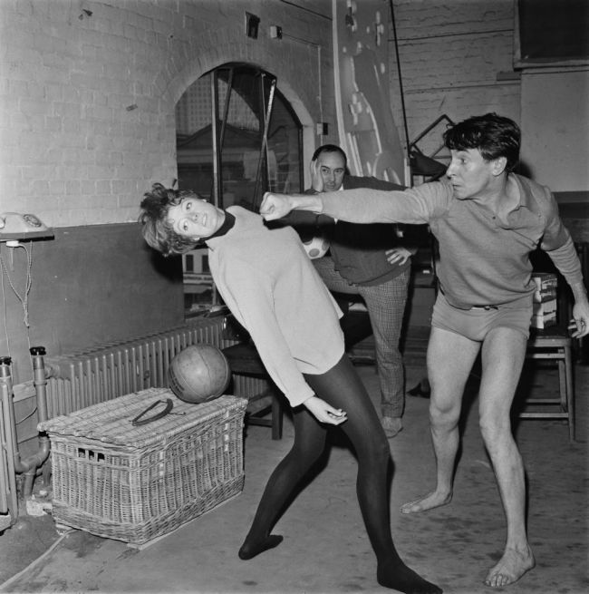 English actor Robert Stephens throws a stage punch at actress Maggie Smith, watched by theatre director John Dexter (1925 - 1990), during a rehearsal for a National Theatre production, UK, 20th April 1966.