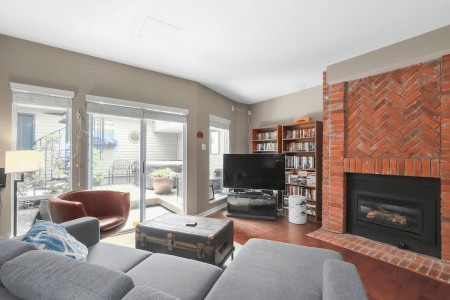 A living room with a fireplace, a TV, a coffee table chest, a couch, and a red chair. A Kitsilano, Vancouver Airbnb.