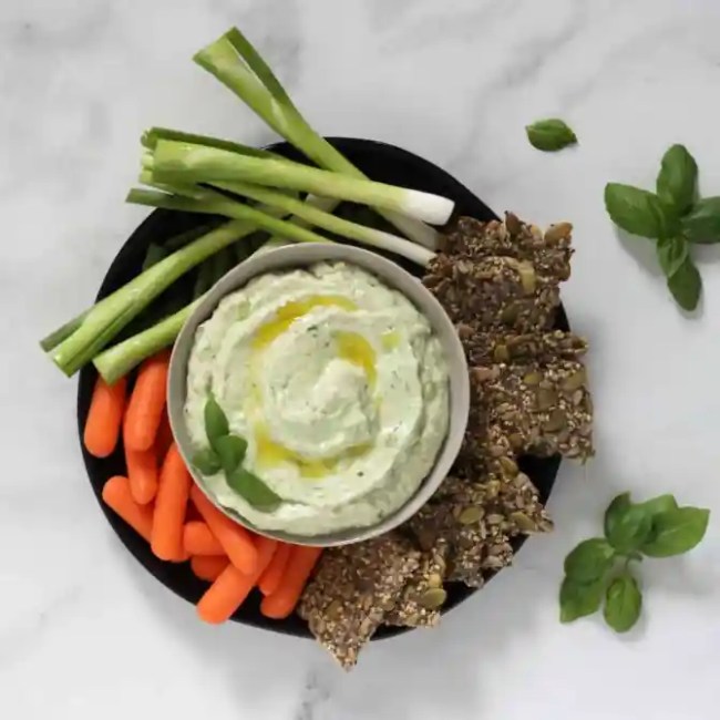 A bowl of celery, carrots, crackers, and avocado dip