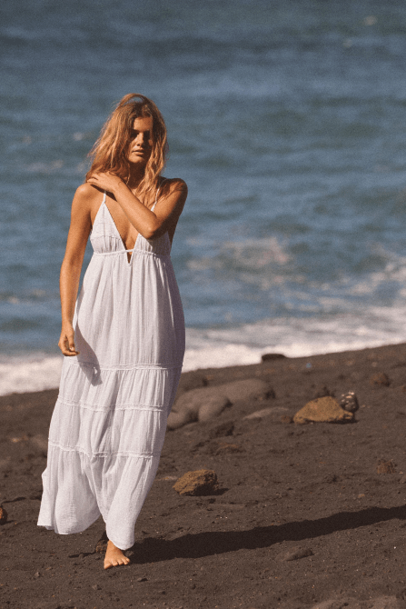 A model walking on the beach wearing the Zara Embroidered Gauze Midi Dress in white
