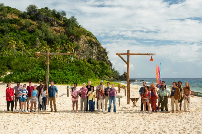 The full cast of Survivor 50 standing on the island in their original tribes.